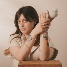 Load image into Gallery viewer, Female, Brunette, whelk top studs, mako tooth ring, limpet ring, whelk wave ring, scallop cuff, twisted bangle, sand dollar cuff, great white tooth cuff, sandy, beige, neutral background