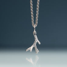 Load image into Gallery viewer, A silver chain necklace with a textured, branch-like pendant, suspended against a dark blue gradient background with a soft reflection below.