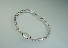 Load image into Gallery viewer, A polished silver chain bracelet with a smooth, oval central plate and a lobster clasp, displayed on a light gray reflective surface.