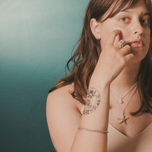 Load image into Gallery viewer, Woman with a tattoo on her arm against a teal background