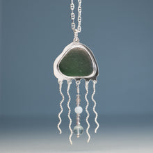 Load image into Gallery viewer, A silver pendant necklace featuring a polished green sea glass cabochon in an organic shape, with dangling wavy silver chains and beads, shown against a soft blue-gray gradient background.