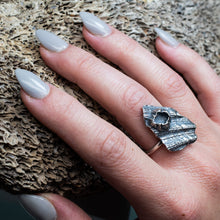 Load image into Gallery viewer, cast darkened metal textural ring with barnacle on hand model with textured beige coral background