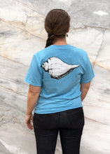 Load image into Gallery viewer, Person wearing a blue t-shirt with a shell graphic and text on the back, standing against a marble wall.