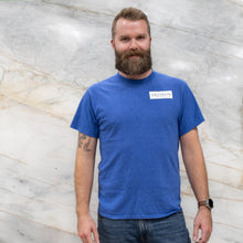 Load image into Gallery viewer, Man wearing a blue t-shirt with a logo against a marble wall
