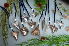 Load image into Gallery viewer, Decorative ornaments with metallic finishes on blue ribbons against a light background with greenery.