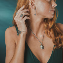 Load image into Gallery viewer, Woman wearing silver jewelry including earrings, necklace, and bracelet against a teal background