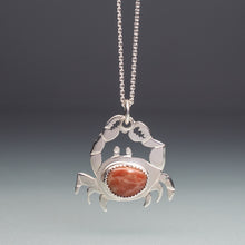 Load image into Gallery viewer, Silver crab pendant with a red stone on a chain against a gradient background