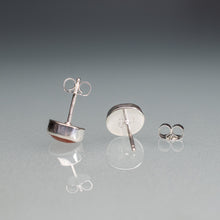 Load image into Gallery viewer, Silver stud earrings on a reflective gray surface with a gradient background