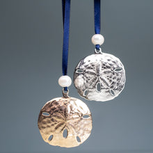 Load image into Gallery viewer, cast bronze and silver sand dollar ornament from stone harbor nj with freshwater pearl and navy blue satin ribbon by hkm jewelry hanging on seafoam background