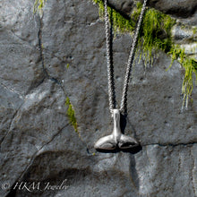 Load image into Gallery viewer, top side of silver dolphin tail necklace by hkm jewelry on a jetty rock with alage