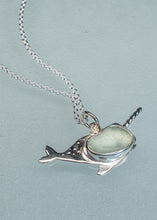 Load image into Gallery viewer, A sterling silver narwhal pendant necklace with a smooth, light green-blue stone set in its head, displayed on a textured light blue-gray background.