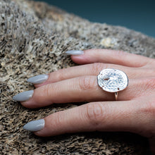 Load image into Gallery viewer, silver sand dollar ring on hand model with grey nails and textured beige coral background
