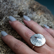 Load image into Gallery viewer, silver sand dollar ring on hand model with grey nails and textured beige coral background