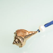 Load image into Gallery viewer, close up detail of cast bronze lightning whelk ornament from key west florida with freshwater pearl and navy blue satin ribbon by hkm jewelry on blue background