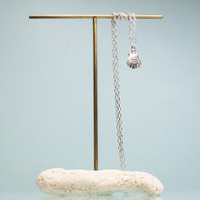 Load image into Gallery viewer, small lions paw scallop shell necklace in polished sterling silver on coral and brass jewelry stand by hkm jewelry