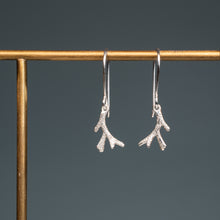 Load image into Gallery viewer, A pair of silver drop earrings with textured coral branch-like dangles, hanging from a gold-tone display stand against a dark gray background.
