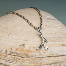 Load image into Gallery viewer, A silver-toned branch-shaped pendant necklace resting on a light beige seashell, with a soft blue-gray background.
