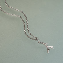 Load image into Gallery viewer, A silver chain necklace with a textured branch-shaped pendant, displayed on a matte sage green background.

