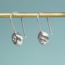 Load image into Gallery viewer, Silver spiral earrings on a gold hook against a teal background
