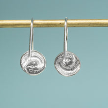 Load image into Gallery viewer, Silver coin earrings hanging from a rod against a teal background
