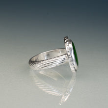 Load image into Gallery viewer, A silver ring with a textured, twisted band and a round bezel-set green stone, shown on a reflective gray surface against a gradient gray background.
