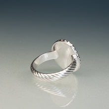 Load image into Gallery viewer, A silver ring with a twisted cable band and a smooth oval face, photographed on a reflective gray surface against a dark gradient background.
