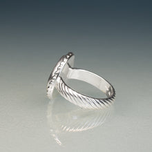 Load image into Gallery viewer, A silver ring with a textured, twisted cable-like band and a circular top, photographed on a reflective gray surface against a dark gradient background.
