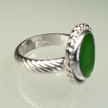 Load image into Gallery viewer, A sterling silver ring featuring a textured, twisted cable band and a large oval green stone, photographed on a light green reflective surface.
