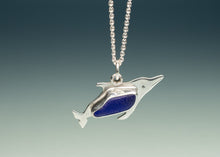 Load image into Gallery viewer, A silver dolphin pendant necklace with a polished blue inlay, suspended from a silver ball chain against a dark blue gradient background.
