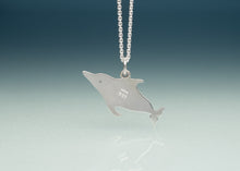 Load image into Gallery viewer, A silver dolphin pendant necklace on a silver ball chain, displayed against a blue gradient background with a soft reflection below.
