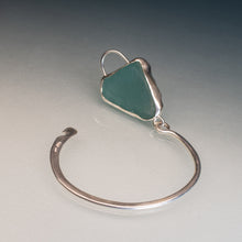 Load image into Gallery viewer, A sterling silver open cuff bangle featuring a triangular sea glass charm in a muted teal green color, displayed on a neutral gray gradient background.
