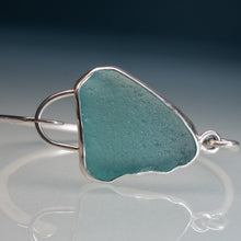 Load image into Gallery viewer, A sterling silver ring featuring a large, irregularly shaped piece of turquoise sea glass, displayed on a reflective surface against a dark blue gradient background.
