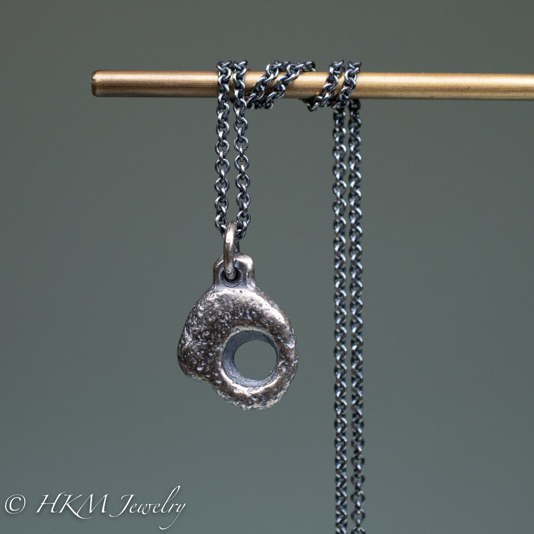 close up of hag stone necklace cast in sterling silver by hkm jewelry in oxidized finish