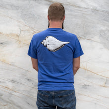 Load image into Gallery viewer, Man wearing a blue t-shirt with a white shell design on the back, standing against a marble wall.
