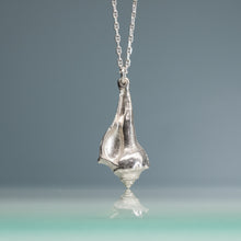 Load image into Gallery viewer, Silver knobbed whelk shell pendant on a chain against a gradient blue green background
