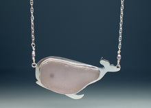 Load image into Gallery viewer, A whale-shaped pendant necklace featuring a smooth, pale pinkish-gray stone inlay set in polished silver-tone metal, suspended from a delicate silver chain against a dark blue gradient background.
