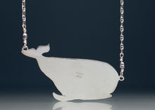 Load image into Gallery viewer, A polished silver whale-shaped pendant necklace on a matching silver chain with small purple beads, shown against a dark navy background.
