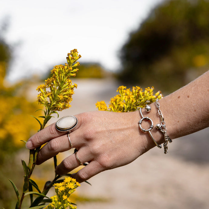 Hand with rings and bracelets holding yellow flowers against a blurred natural background image by susan allen