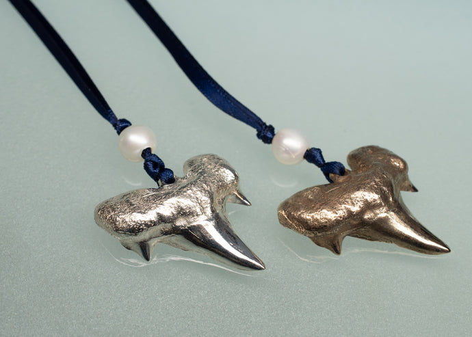 Two shark tooth ornaments on blue cords with pearls against a light gray background