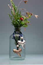 Load image into Gallery viewer, Decorative glass bottle with floral arrangement and decorative elements on a gray background
