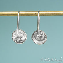 Load image into Gallery viewer, Silver earrings with circular designs hanging on a rod against a teal background, branded with HKM Jewelry.
