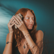 Load image into Gallery viewer, Woman with red hair holding a stone against a blue background
