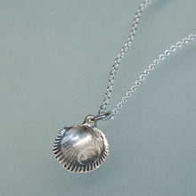 Load image into Gallery viewer, A sterling silver scallop shell pendant necklace on a delicate silver chain, displayed on a soft, muted blue-gray background.
