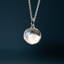 Load image into Gallery viewer, A silver pendant necklace featuring a textured, scalloped shell-shaped charm on a matching chain, set against a dark blue gradient background.
