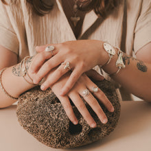 Load image into Gallery viewer, Close-up of hands with multiple rings and bracelets on a textured surface
