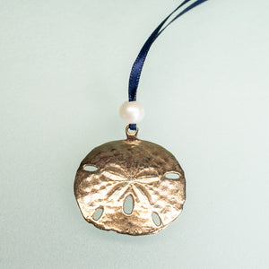 cast bronze sand dollar ornament from stone harbor nj with freshwater pearl and navy blue satin ribbon by hkm jewelry on seafoam background