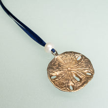 Load image into Gallery viewer, backside view of cast bronze sand dollar ornament from stone harbor nj with freshwater pearl and navy blue satin ribbon by hkm jewelry 
