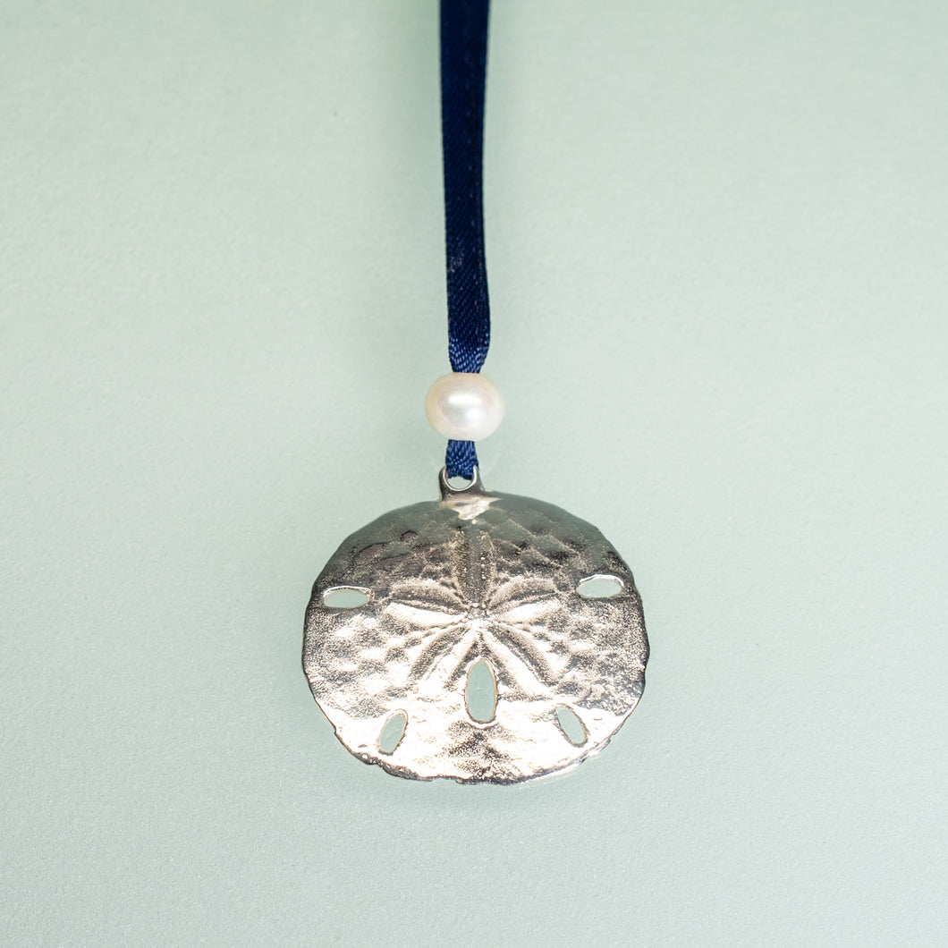 cast silver sand dollar ornament from stone harbor nj with freshwater pearl and navy blue satin ribbon by hkm jewelry on blue background