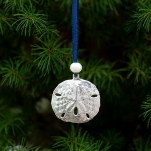 close up of cast silver sand dollar ornament from stone harbor nj with freshwater pearl and navy blue satin ribbon by hkm jewelry on evergreen tree