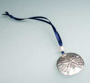 cast silver sand dollar ornament from stone harbor nj with freshwater pearl and navy blue satin ribbon by hkm jewelry on blue background